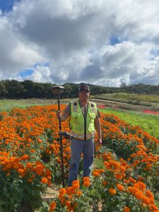 Crew Chief Jared Nielsen stands confidently in a professional pose, wearing work attire and a reflective vest. With a backdrop of a construction site, the image highlights leadership, professionalism, and dedication to the field.