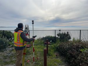 Crew Chief Jared Nielsen stands confidently atop a cliff overlooking Monterey Bay, with a serene expanse of ocean and sky stretching out in the background. The scene captures leadership, focus, and the natural beauty of the California coastline.