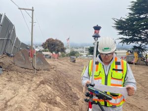 Crew Chief Jared Nielsen reviews construction drawings with focused precision, standing at a job site surrounded by building materials and equipment. The image highlights expertise, attention to detail, and leadership in action.