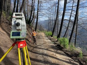 The MCE crew conducts a detailed survey in the Santa Cruz Mountains, surrounded by dense forest and rugged terrain. The image captures teamwork, precision, and adaptability in navigating challenging landscapes.